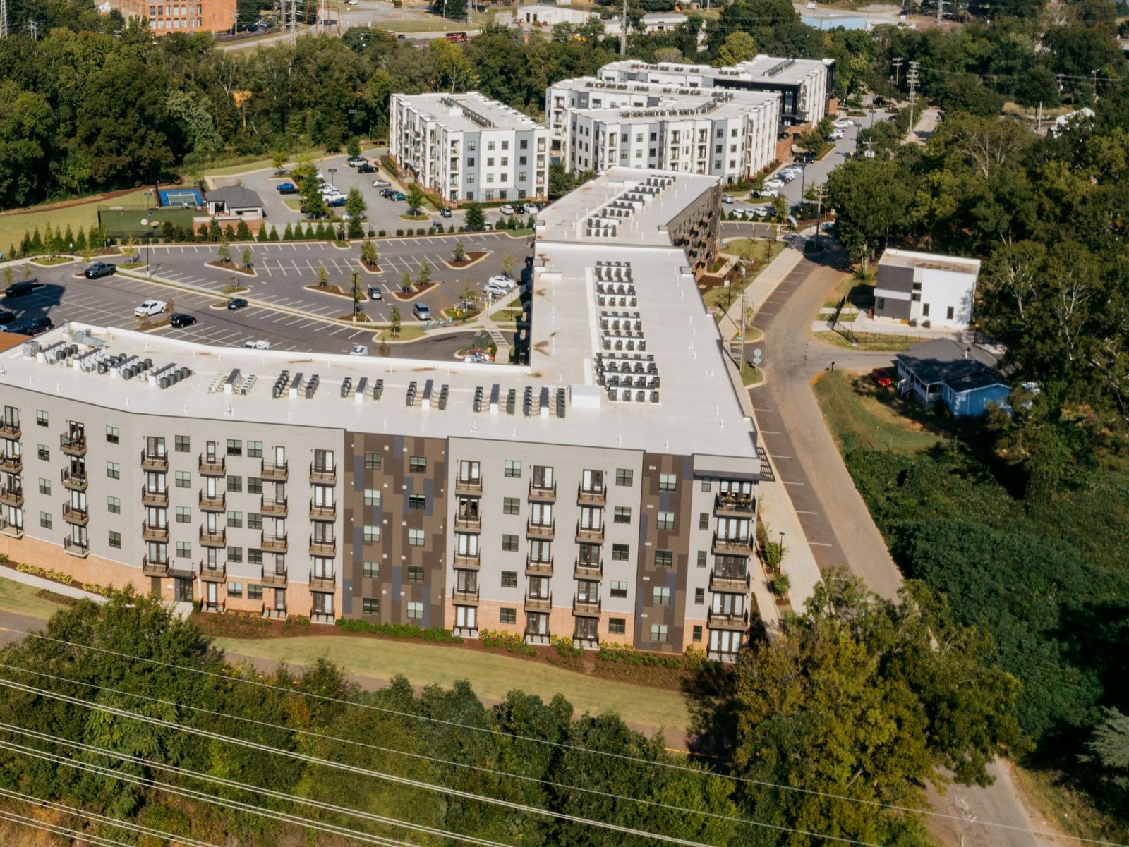 Aerial view of an apartment complex with white low-slope roofs, rows of condensing units set on the roof field and a parking lot below.