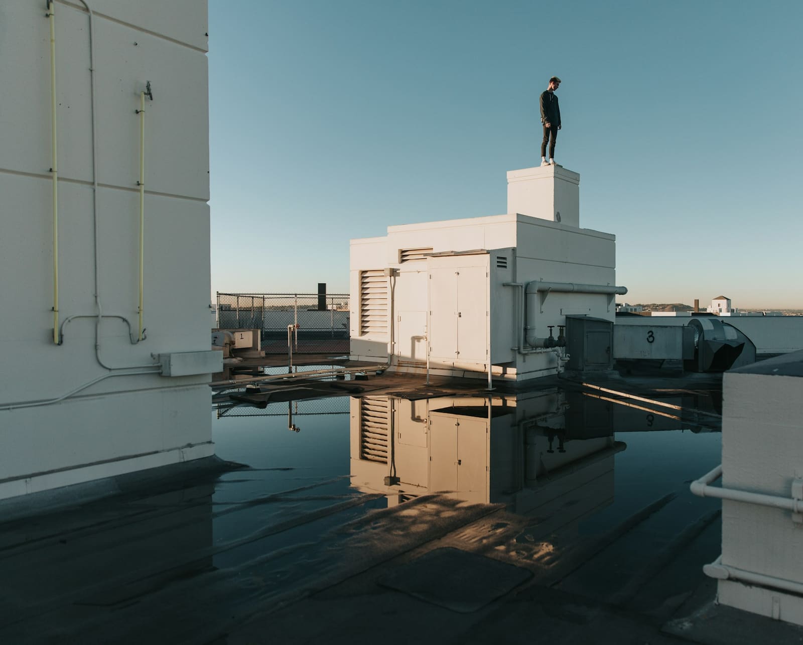 Person standing on a rooftop bulkhead above a flat commercial roof that is holding a wide sheet of standing water around its mechanical equipment.