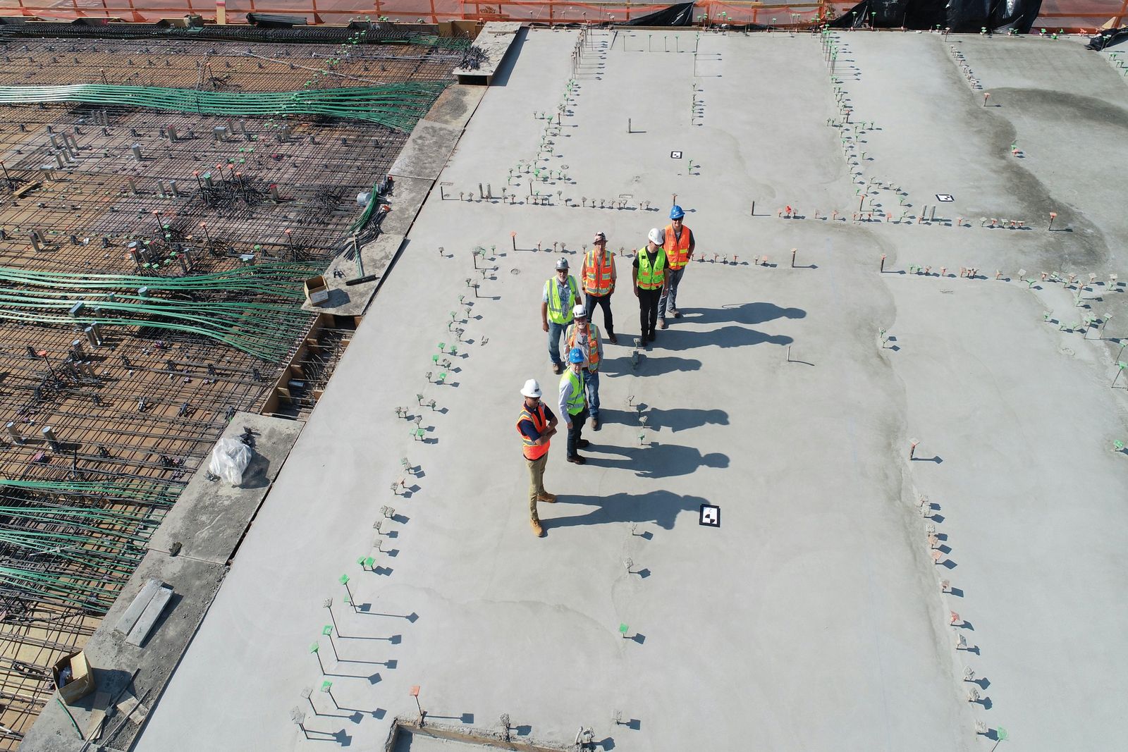 Crew in hard hats and safety vests standing on a bare concrete deck, with reinforcing steel and tendon bundles laid out on the adjoining bay.