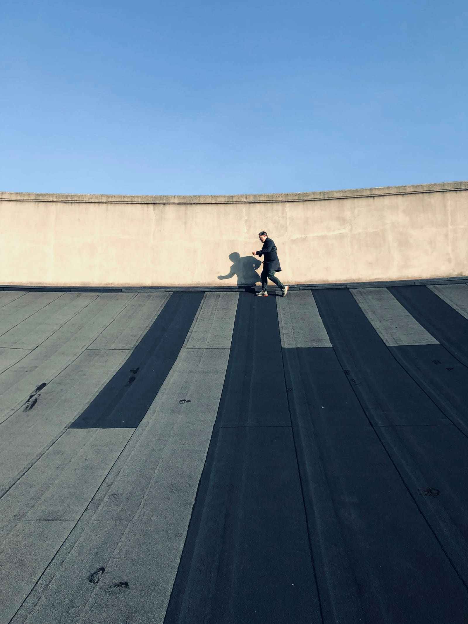 Granule-surfaced low-slope roof field with parallel roll widths running away toward a curved parapet wall.
