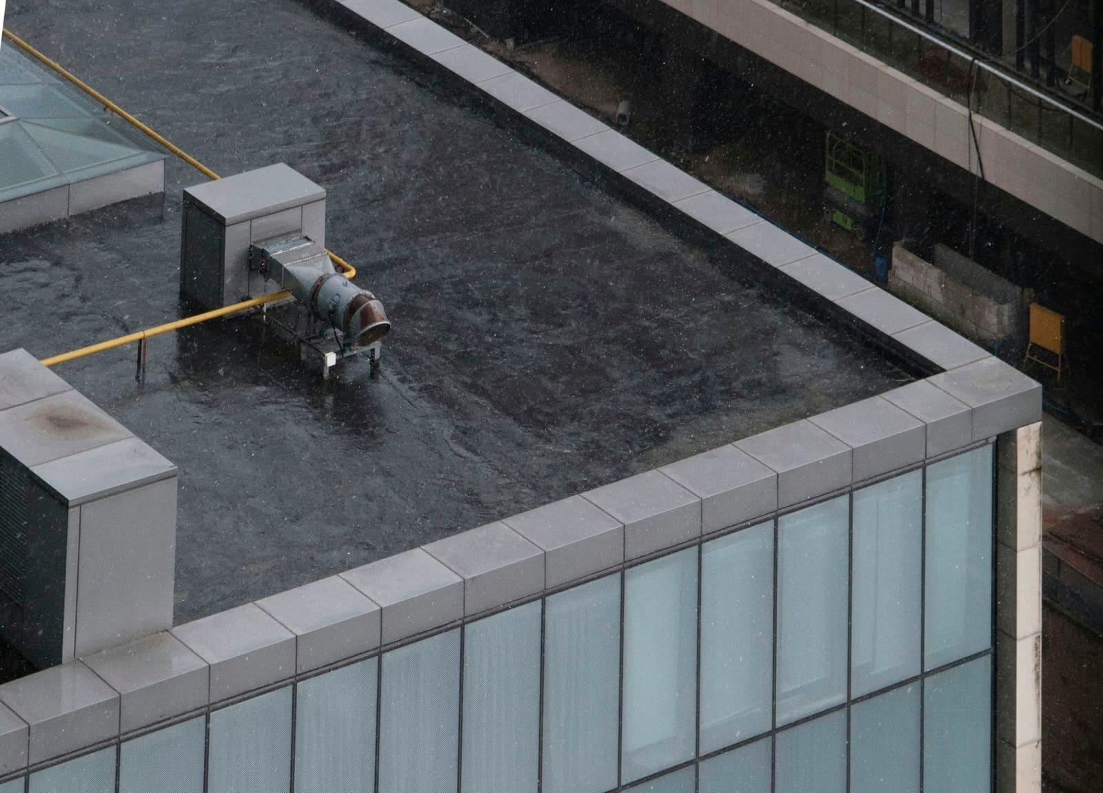 Dark asphalt-surfaced low-slope roof on a commercial building seen from above, with metal coping along the parapet and a rooftop exhaust unit in the field.