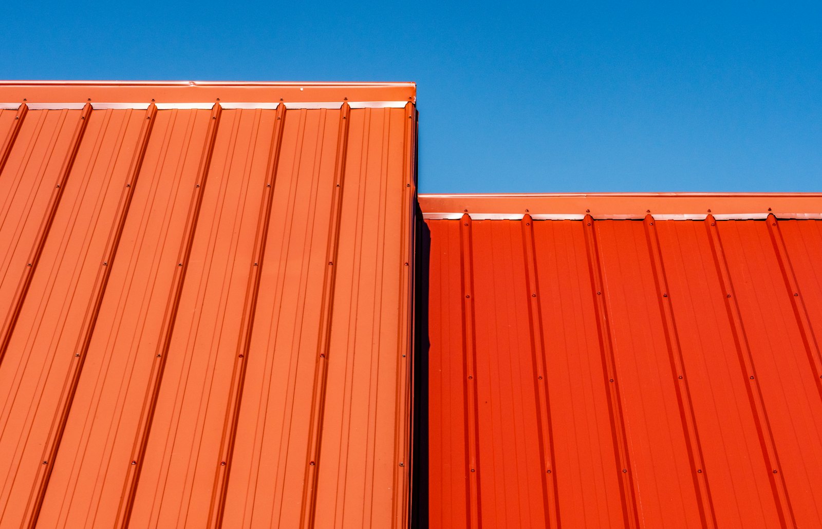 Two adjoining runs of raised-rib metal roof panel stepping down against a clear sky, with the ribs catching the light.